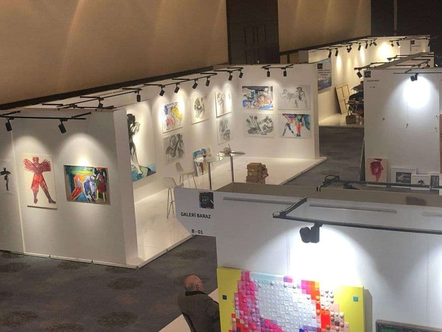 Sanat fuarı alanının yukarıdan görünümü. Odak noktasında "Galeri Baraz B-01" standı ve duvarlarında asılı olan çeşitli tablolar ve çizimler yer alıyor.