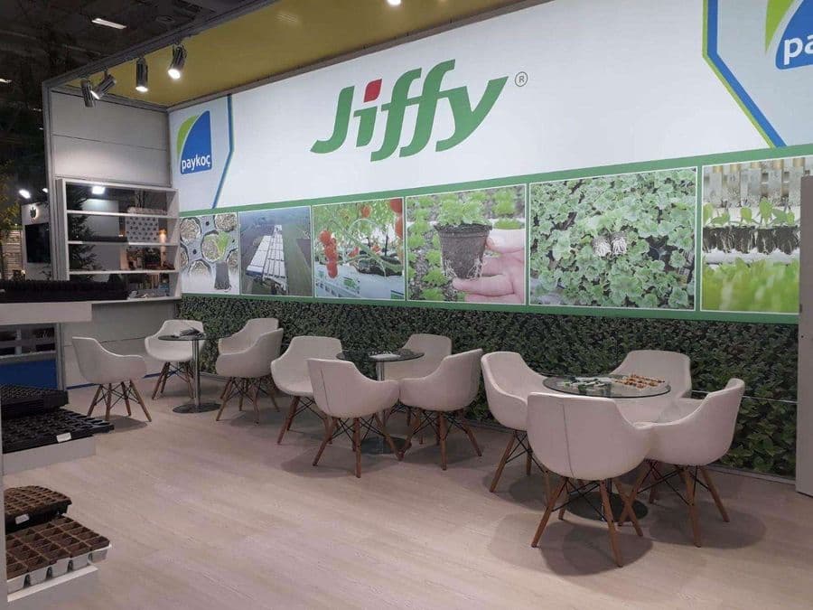 Bahçecilik ürünleri markası "Jiffy"nin bir fuardaki tanıtım standı. Beyaz ve yeşil temalı stantta, bir yanda filizlerin sergilendiği raflar, diğer yanda ise ziyaretçilerin oturduğu masa ve sandalyeler bulunuyor.