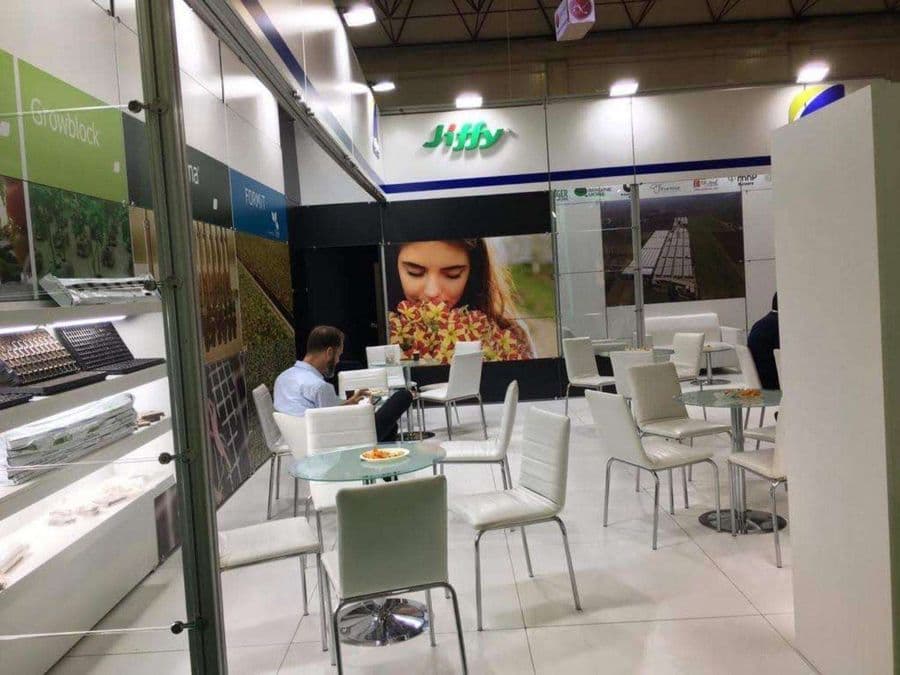 Bahçecilik ürünleri markası "Jiffy"nin bir fuardaki tanıtım standı. Beyaz ve yeşil temalı stantta, bir yanda filizlerin sergilendiği raflar, diğer yanda ise ziyaretçilerin oturduğu masa ve sandalyeler bulunuyor.