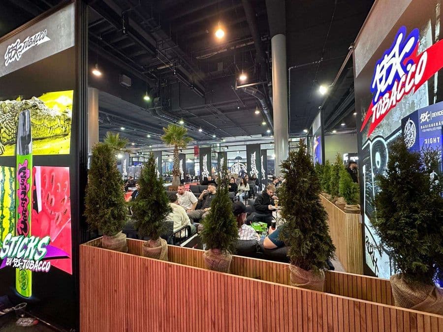 Bir nargile tütünü markasına ait, dinlenme alanı olarak tasarlanmış büyük bir fuar standı. Ahşap paneller ve saksıdaki küçük çam ağaçları ile çevrelenmiş alanda, ziyaretçiler siyah koltuklarda oturup dinleniyor.