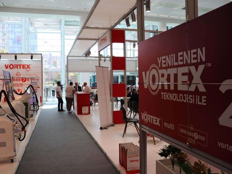 "Vortex Diode Lazer" markasının medikal estetik cihazlarını sergilediği bir fuar standı. Kırmızı ve beyaz temalı stantta, çok sayıda lazer cihazı yan yana dizilerek tanıtılıyor.