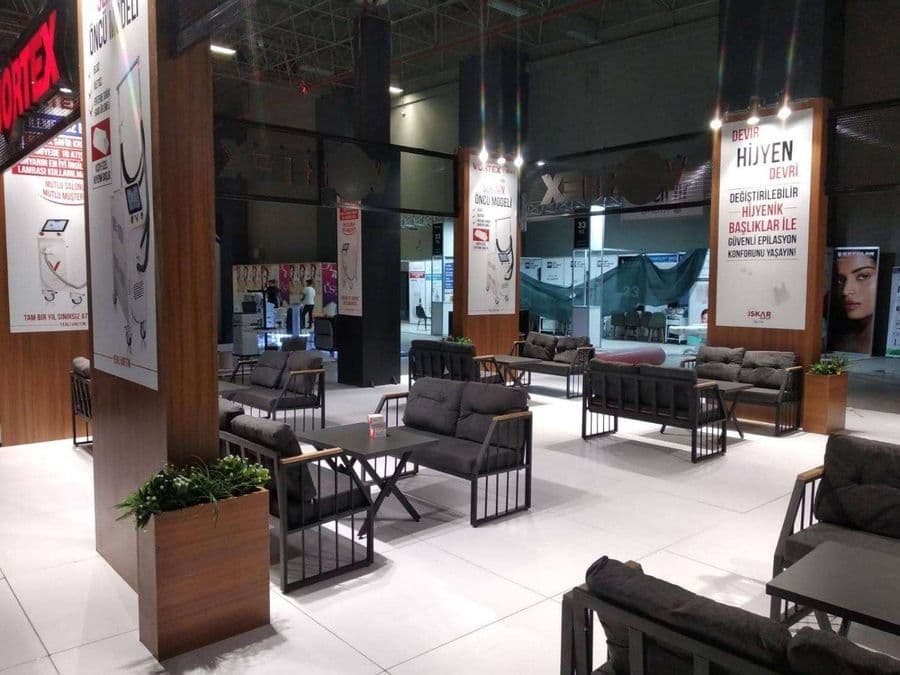 Endüstriyel ürünler fuarında, "VORTEX" markasının modern standı. Işıklı büyük bir logoya sahip standın içi, ziyaretçiler için çok sayıda kanepe ve koltukla bir bekleme alanı gibi tasarlanmış.